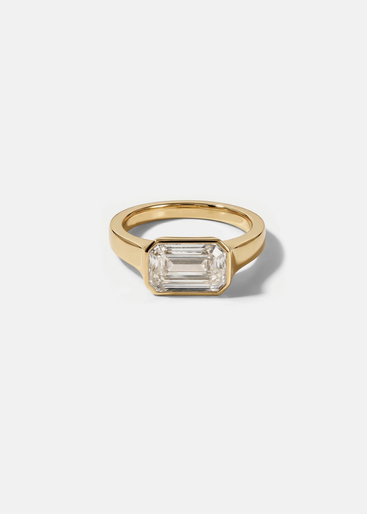 a 18k yellow gold ring with a east west emerald cut diamond as the center stone