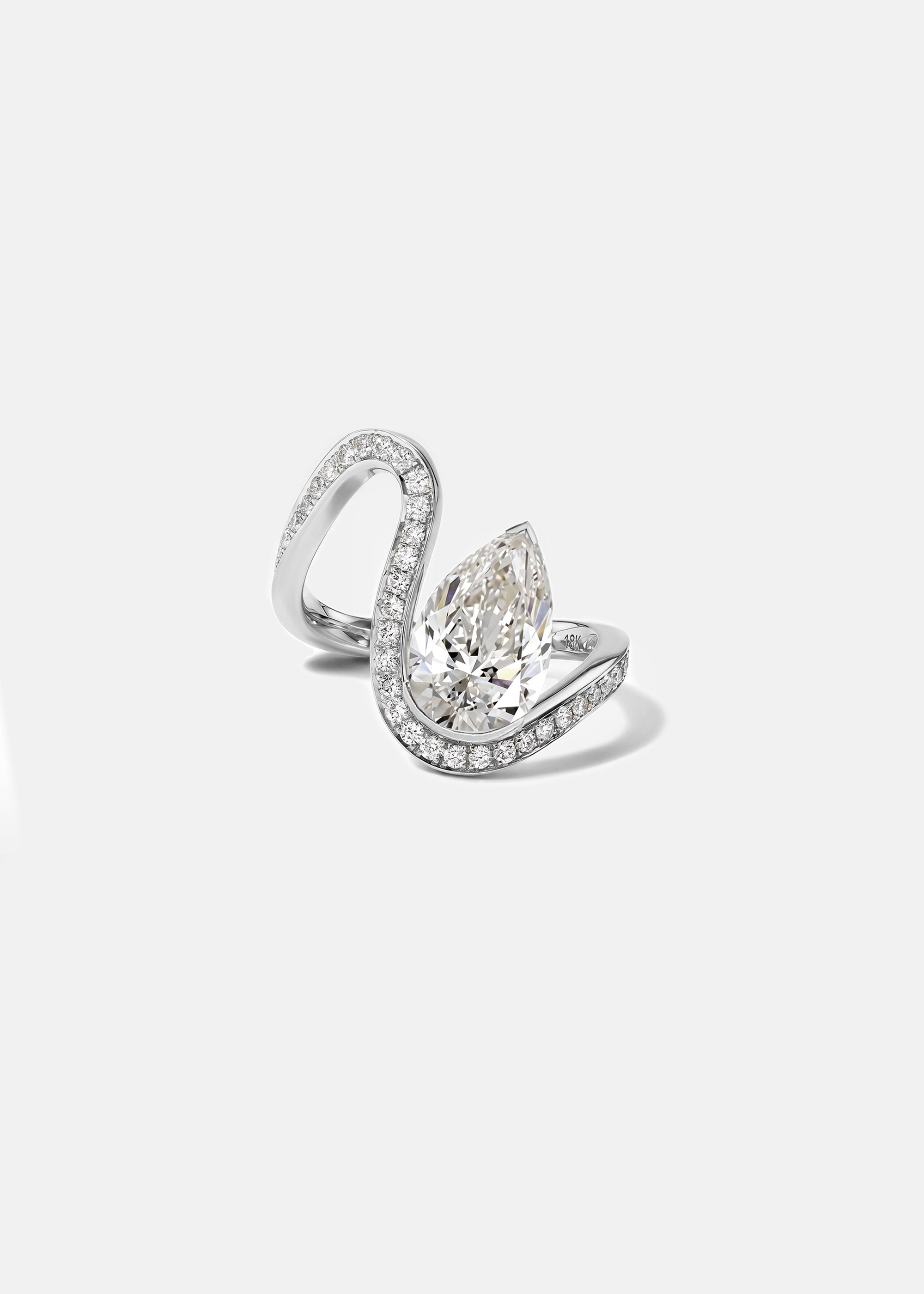 18k white gold trace band with halo of pavé diamonds along the band and a floating pear cut diamond slightly tilted
