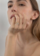 Model wearing a front 18k yellow gold trace band with pavé diamonds and a floating pear cut diamond slightly tilted- on her ring finger
