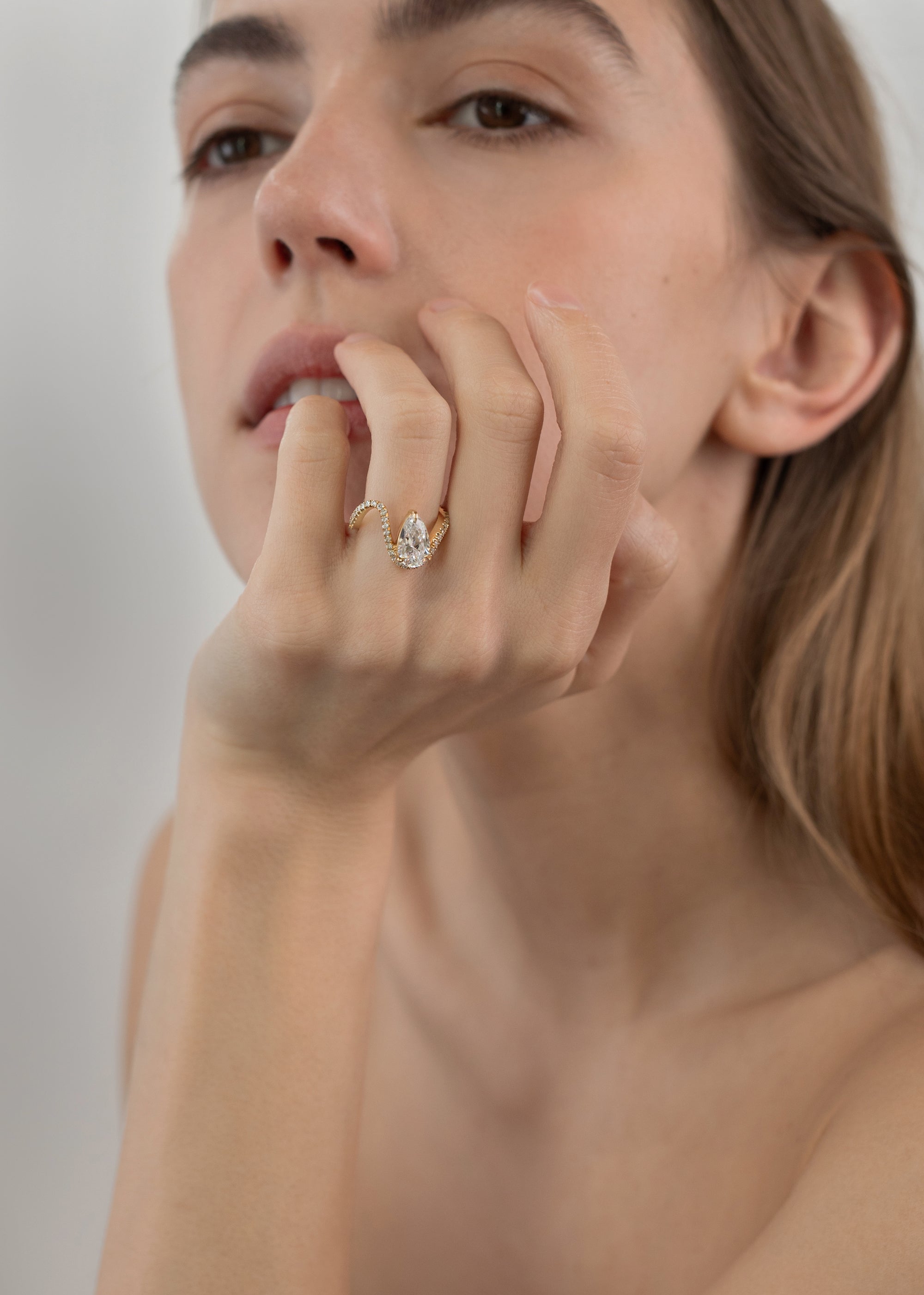 Model wearing a front 18k yellow gold trace band with pavé diamonds and a floating pear cut diamond slightly tilted- on her ring finger
