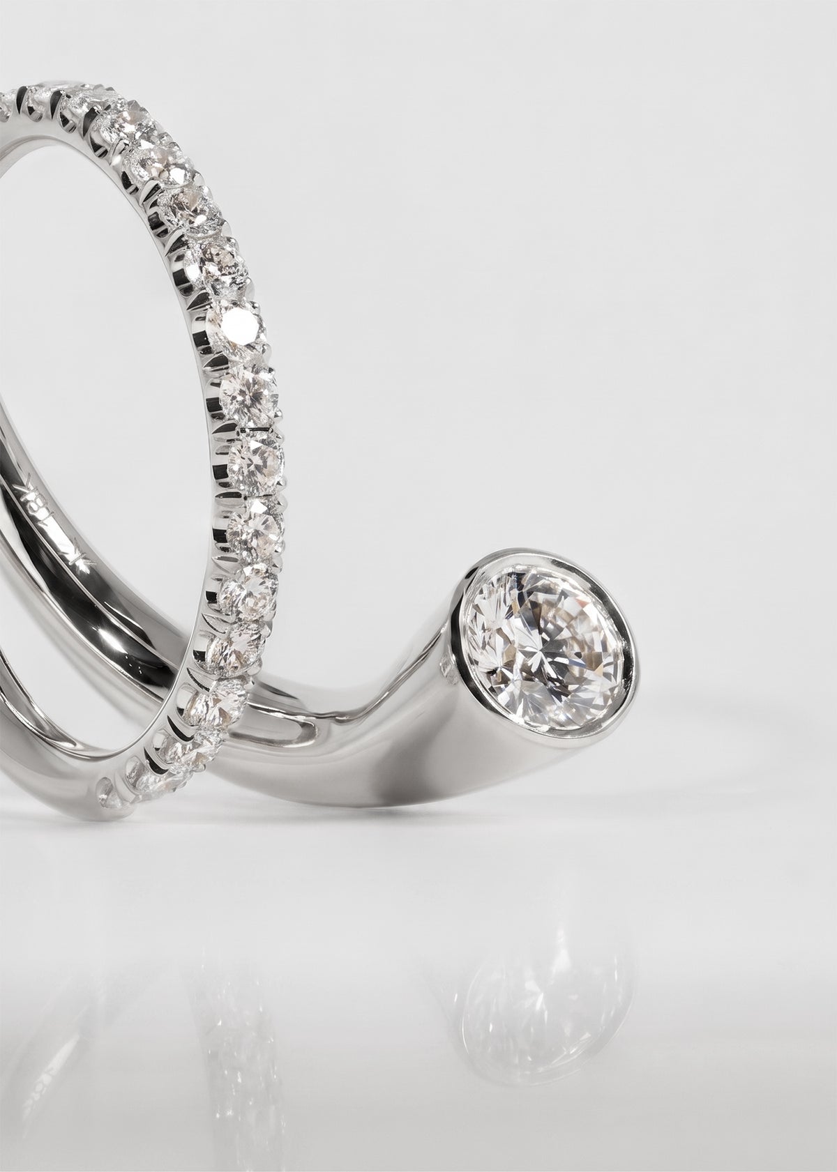 close up of 18k white gold sculptural bypass ring featuring a floating round cut diamond accented by an unexpected tilted band silhouette of pavé diamonds.