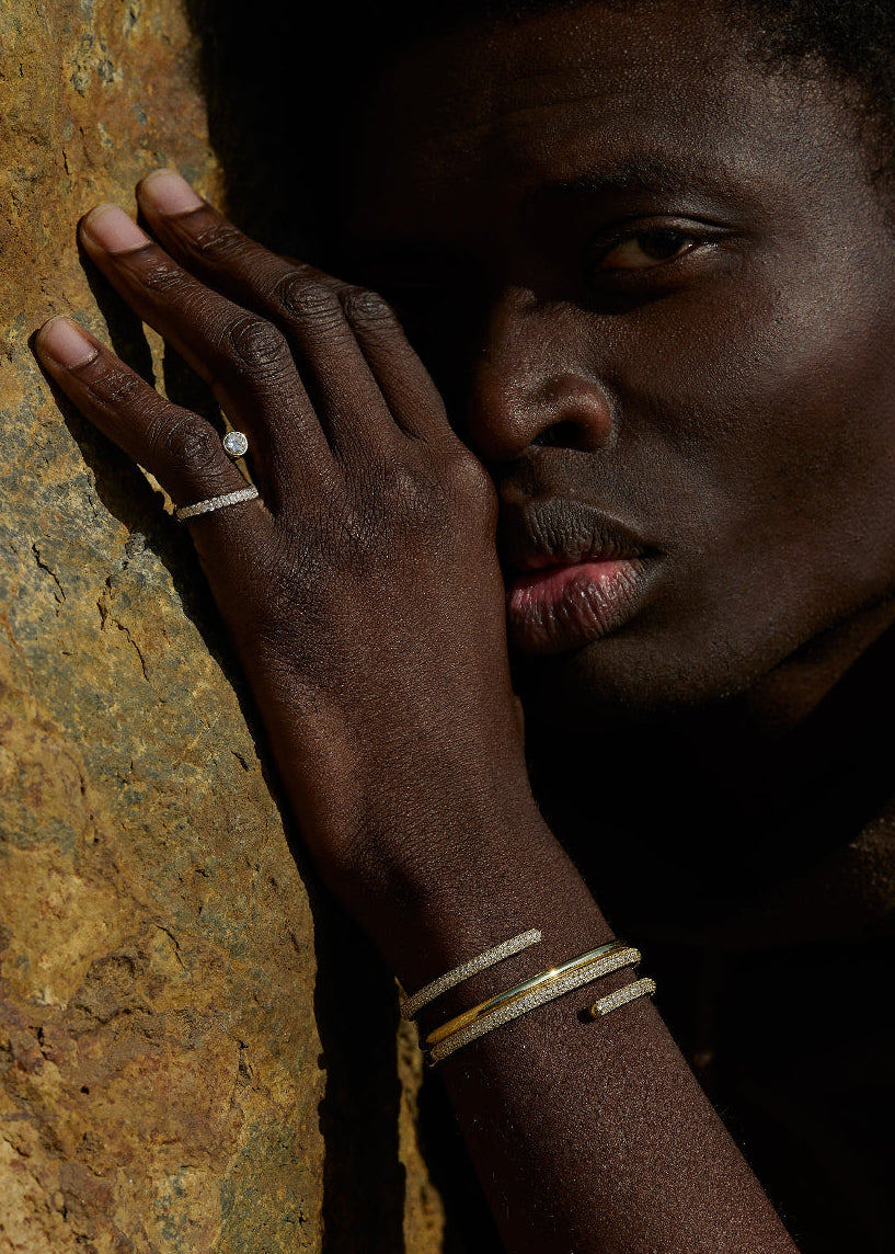 male model wearing 18k yellow gold sculptural bypass ring featuring a floating round cut diamond accented by an unexpected tilted band silhouette with pavé diamonds.