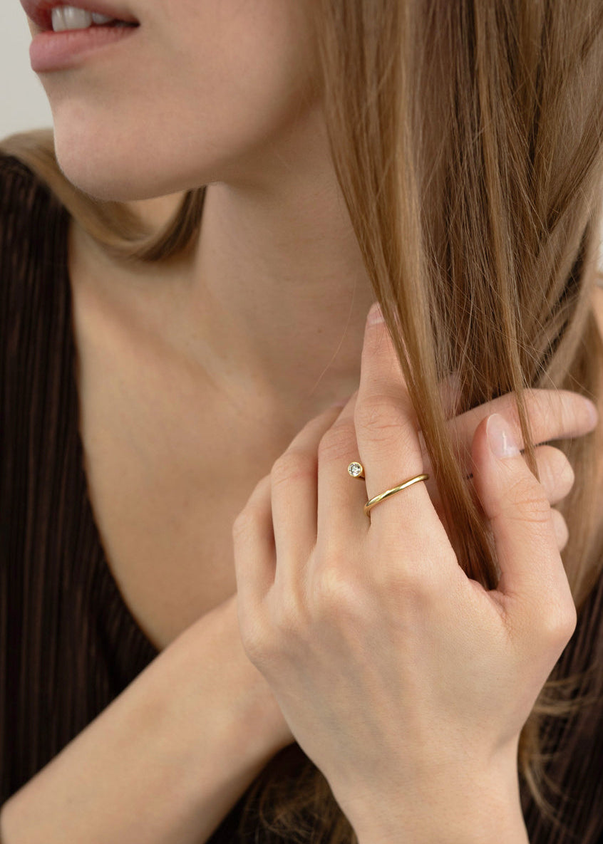 close up of model wearing 18k yellow gold sculptural bypass ring featuring a floating round cut diamond accented by an unexpected tilted band silhouette.