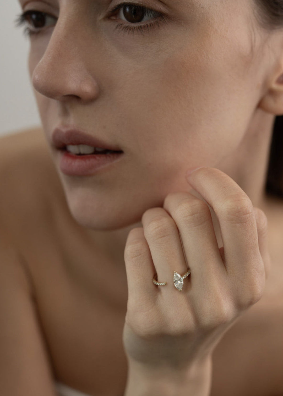 close up of a model's hand wearing 18k yellow gold engagement ring with a floating marquise cut diamond anchored on a tapering micropavé diamond band