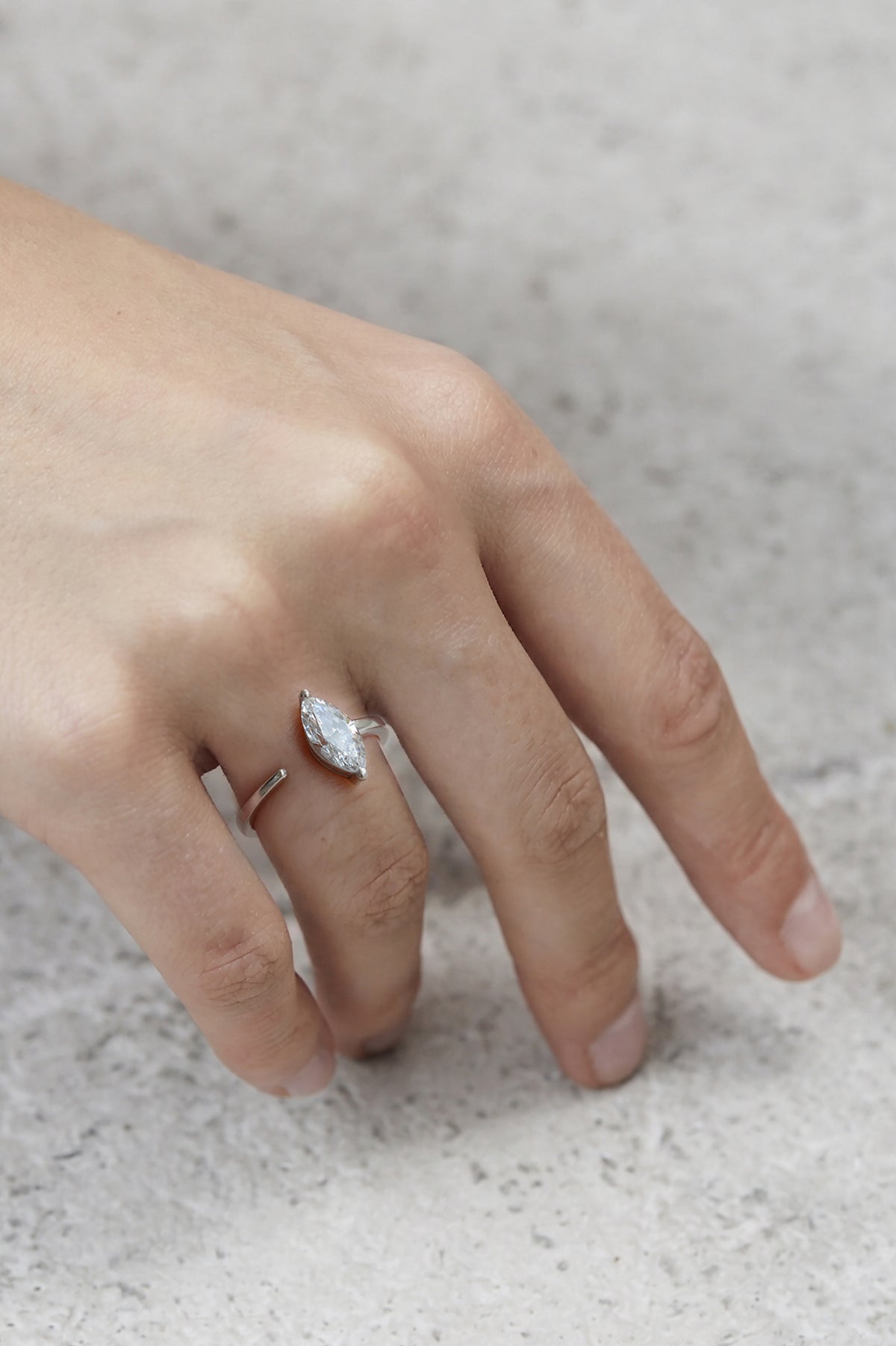 hand wearing a 18k white gold engagement ring with a prong-set marquise diamond anchored on a fluid, tapering open band