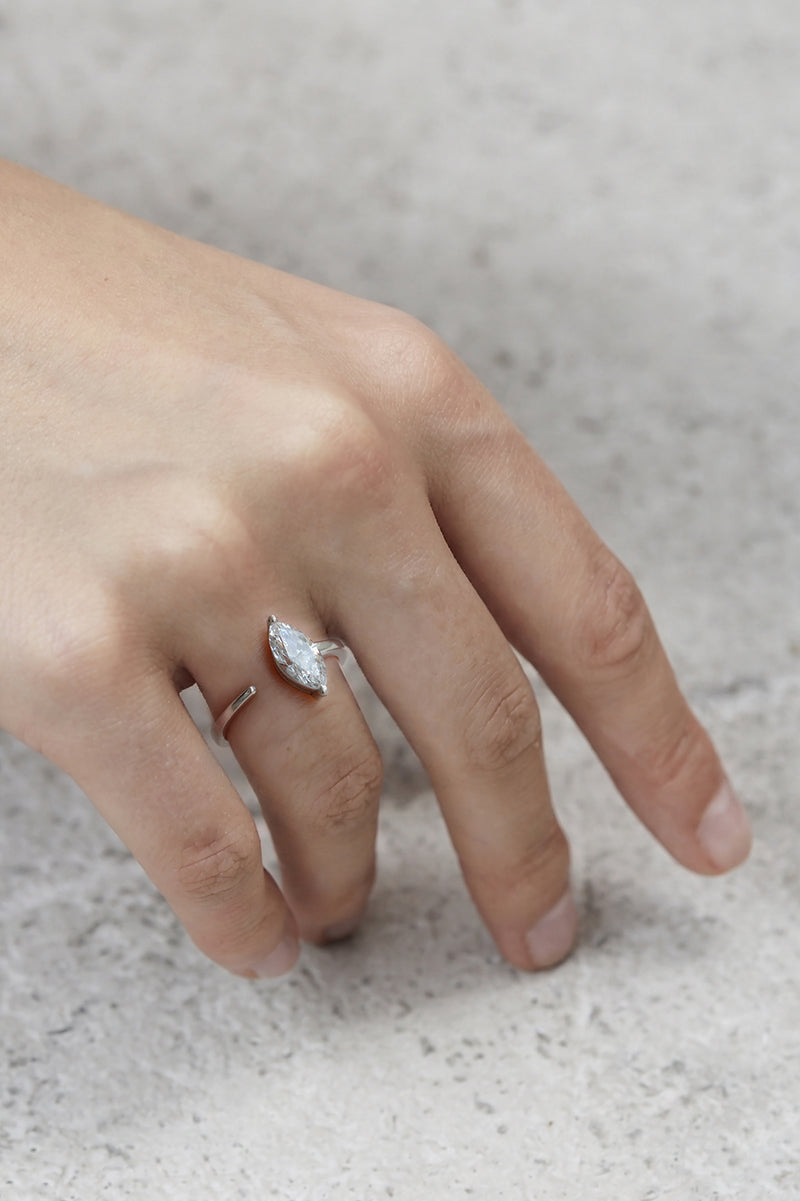hand wearing a 18k white gold engagement ring with a prong-set marquise diamond anchored on a fluid, tapering open band