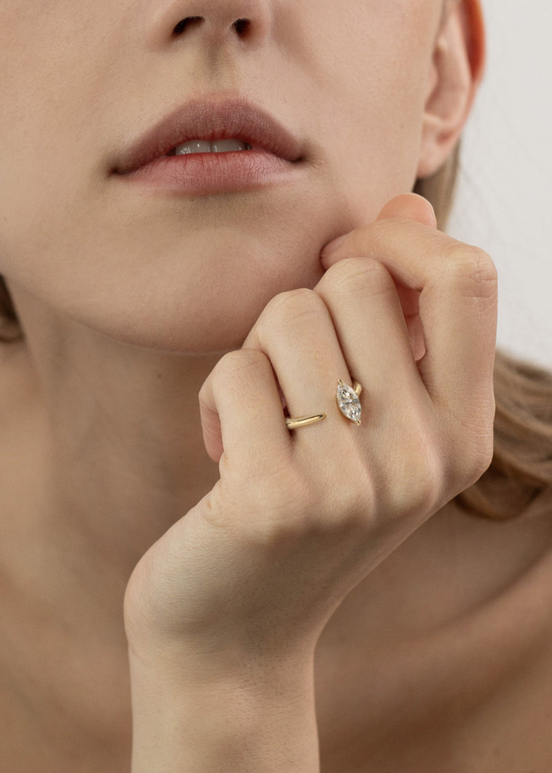 close up of a model's hand wearing a 18k yellow gold engagement ring with a prong-set marquise diamond anchored on a fluid, tapering open band.