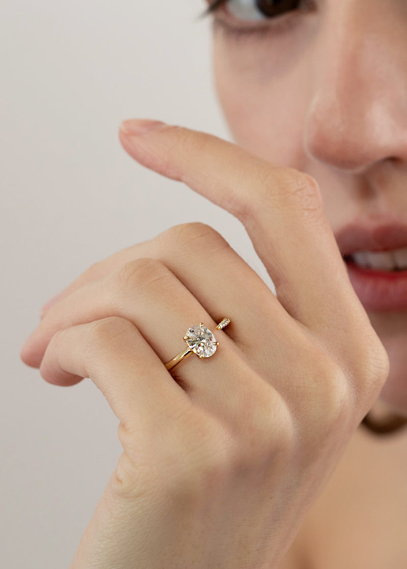 close up of a hand wearing 18k yellow gold Brilliant Crescendo Ring with a floating oval diamond on a tapered open band on her ring finger.