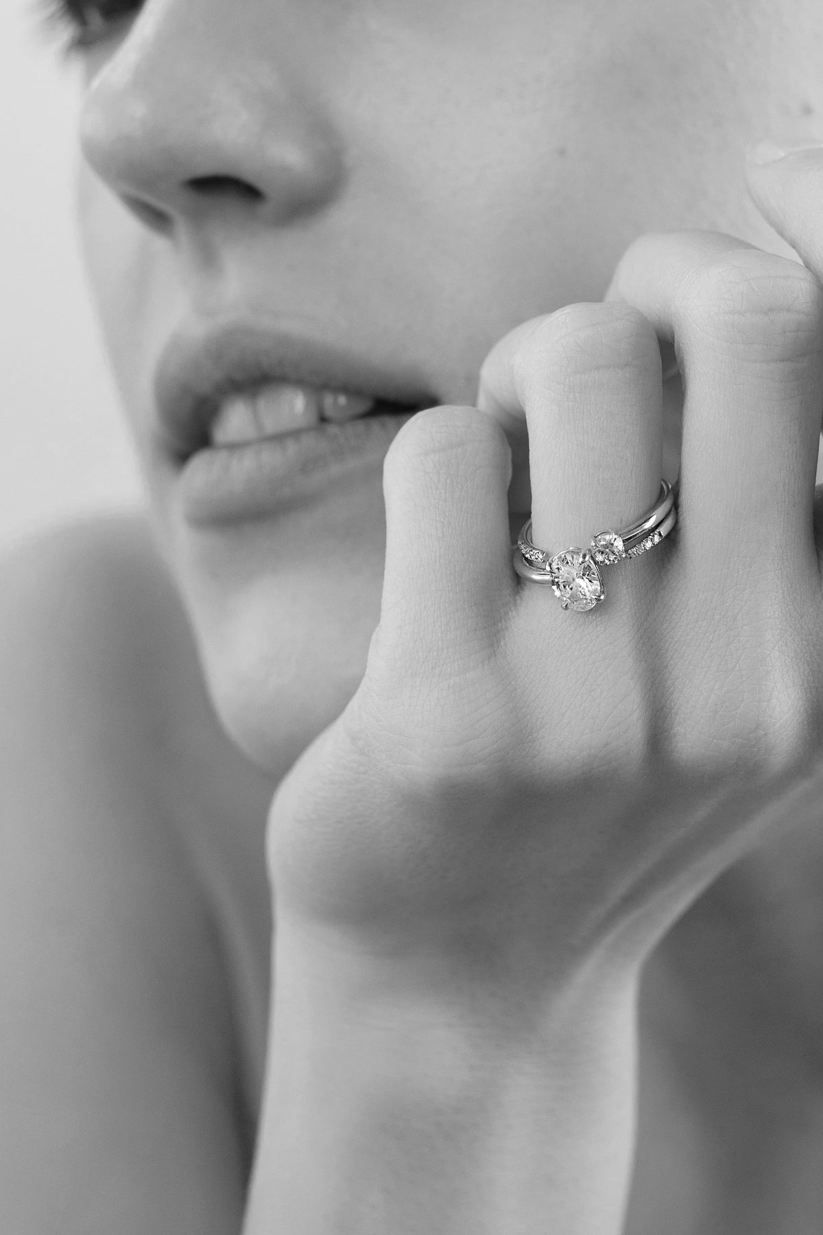 close up of a hand wearing a stack of 18k yellow gold solitaire engagement ring featuring a floating oval diamond on a fluid, tapering open band with a round cut diamond on a gold open band.