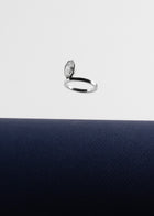 18k white gold engagement ring featuring an elevated floating oval cut diamond in a sculpted octagon bezel setting floating above a dark blue surface