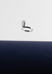 18k white gold engagement ring featuring an elevated floating oval cut diamond in a sculpted octagon bezel setting floating above a dark blue surface