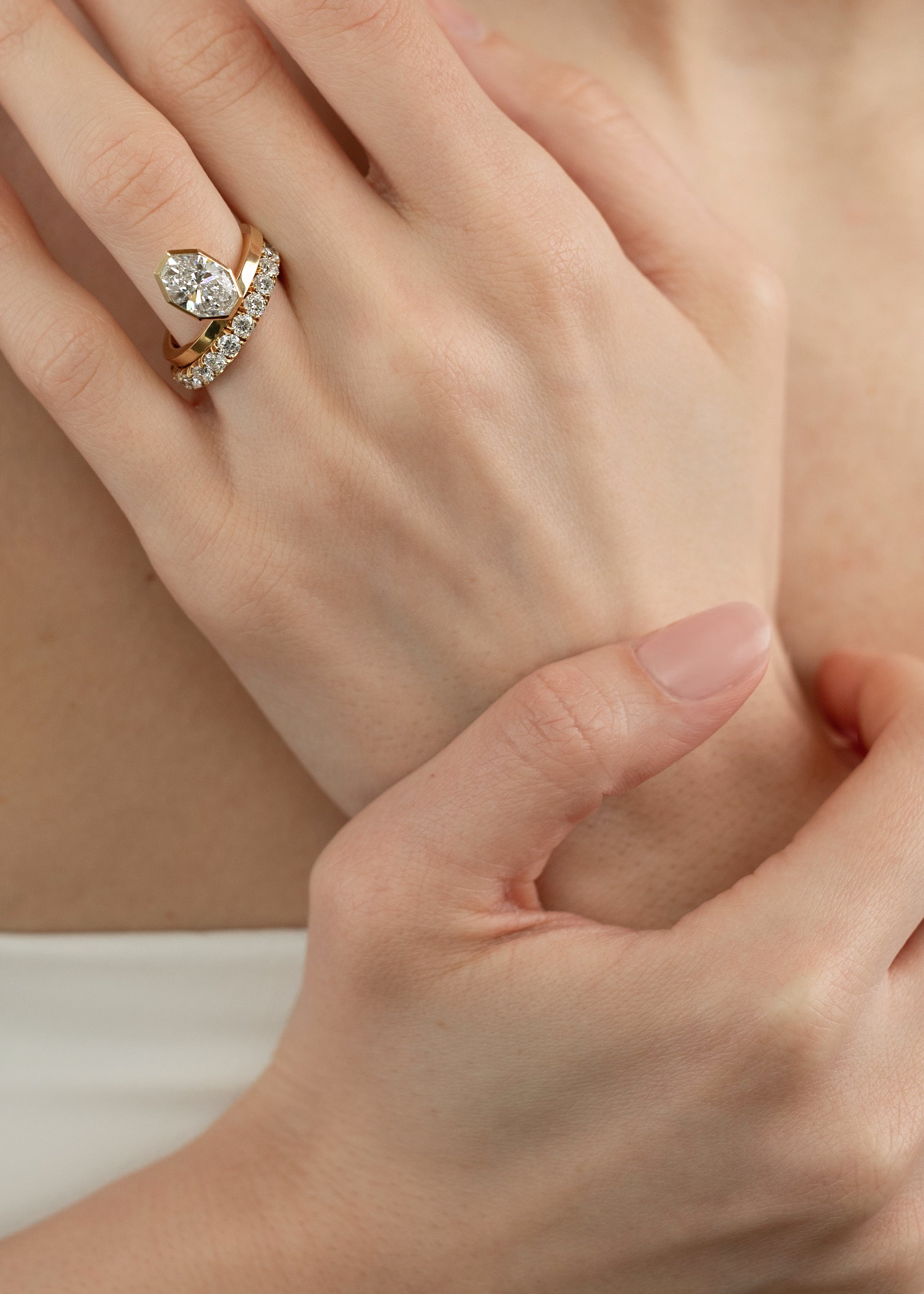 close up of a hand wearing 18k yellow gold engagement ring featuring an elevated floating oval cut diamond in a sculpted octagon bezel setting paired with a diamond band