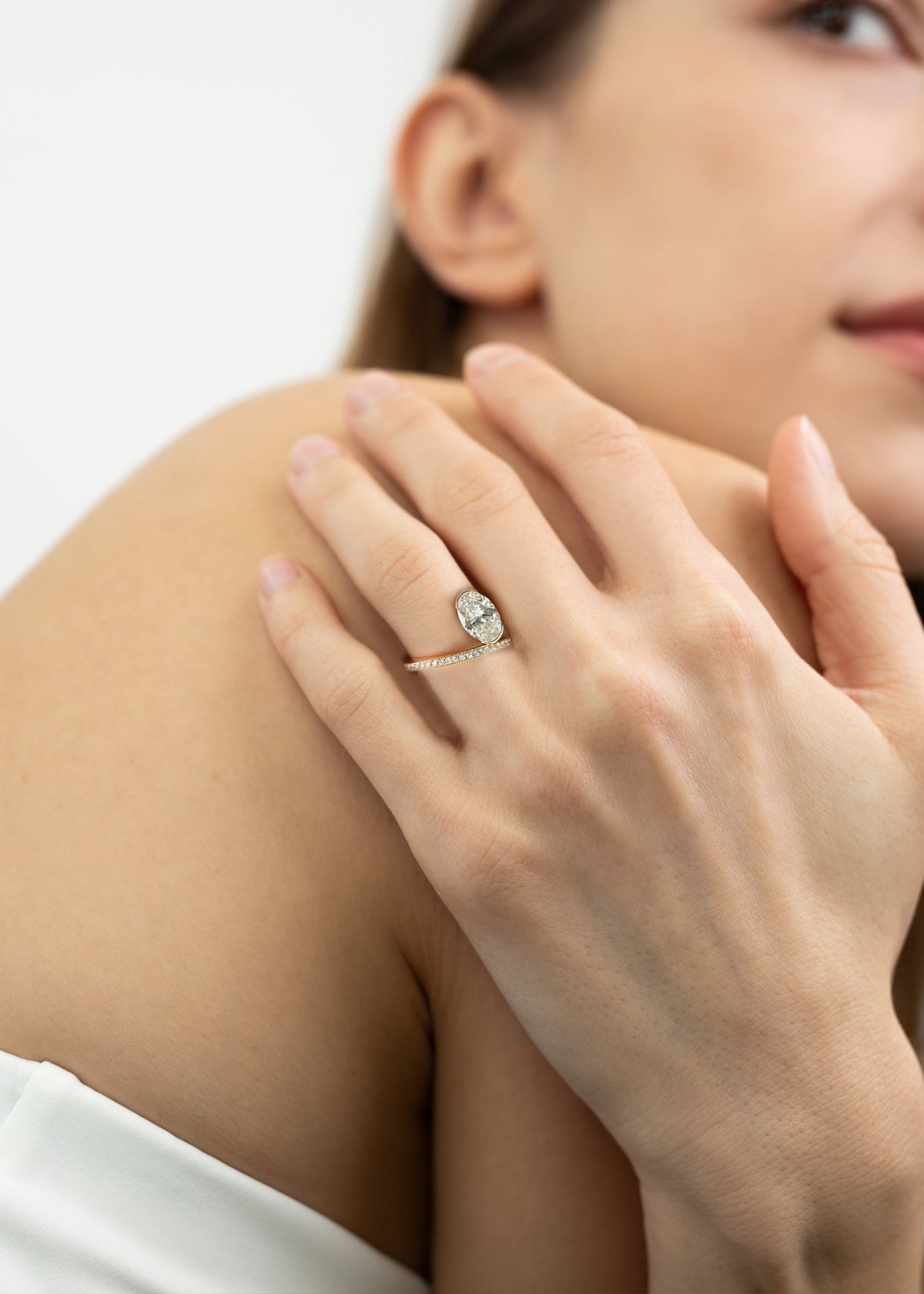 model wearing a 18k yellow gold ring on the rign finger showcasing a fluid line of micro-pavé diamonds that winds continuously around the finger- the design securely cradles a floating, bezel-nested oval diamond along a floating bypass band-KATKIM-engagement ring-fine jewelry