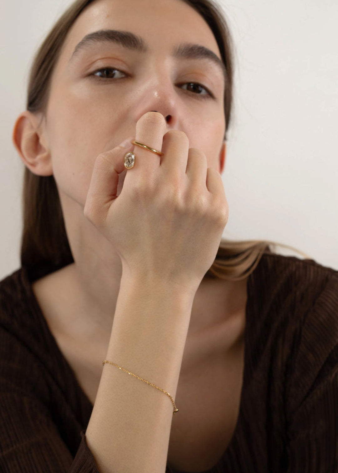 Woman with hand near her mouth wearing a 18k yellow gold Oval Crescendo Flare Ring with a floating oval diamond and tilted wrapping band