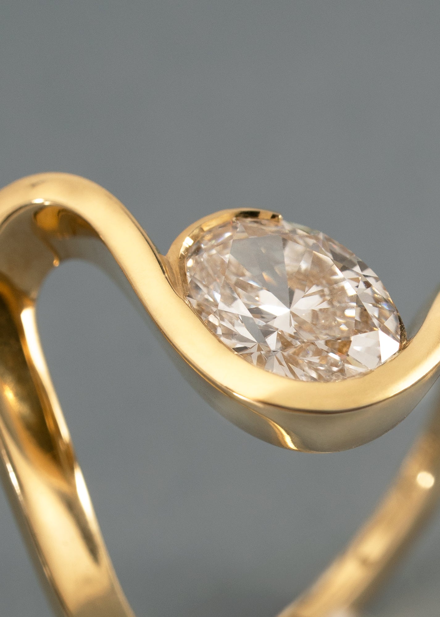 close-up - a 18k yellow gold ring with a wide wavy band resembling a ribbon nestling an oval cut diamond