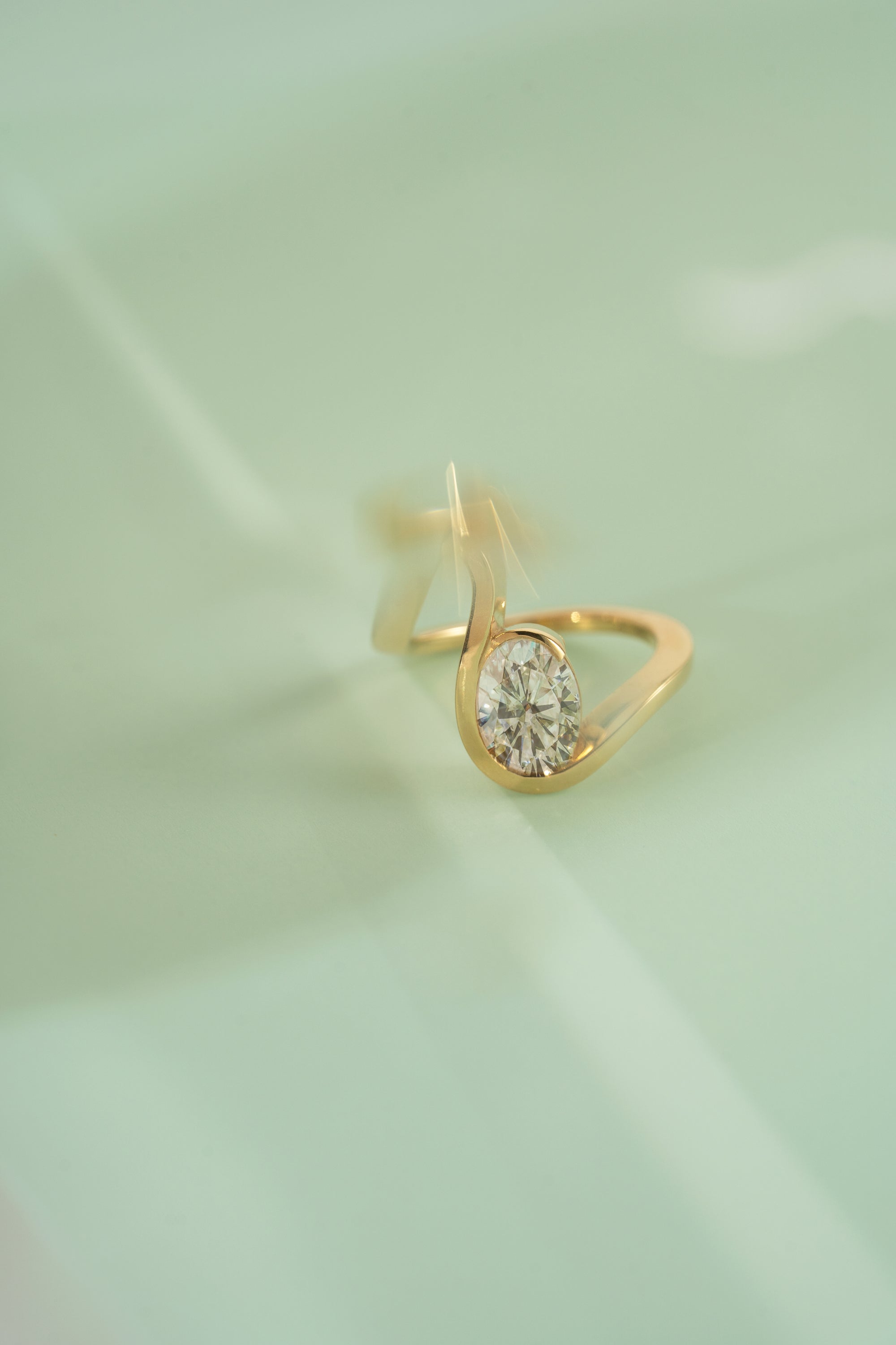 18k yellow gold ring with a wide wavy band resembling a ribbon nestling an oval cut diamond