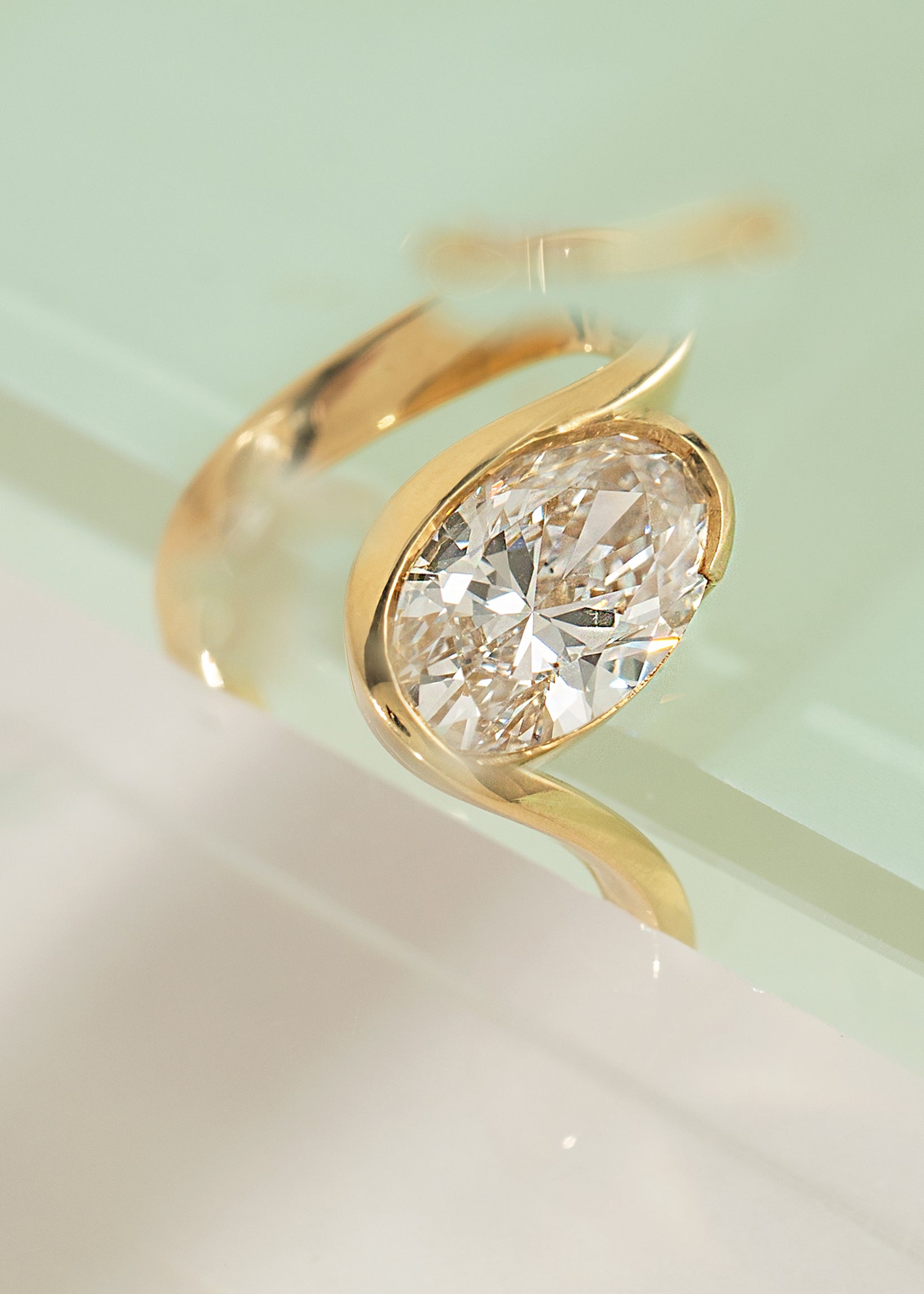 18k yellow gold ring with a wide wavy band resembling a ribbon nestling an oval cut diamond- wedged between two clear acrylic block