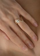 moel wearing a 18k yellow gold ring featuring a large oval diamond with a curved band surrounded by a halo of small pavé-set diamonds.