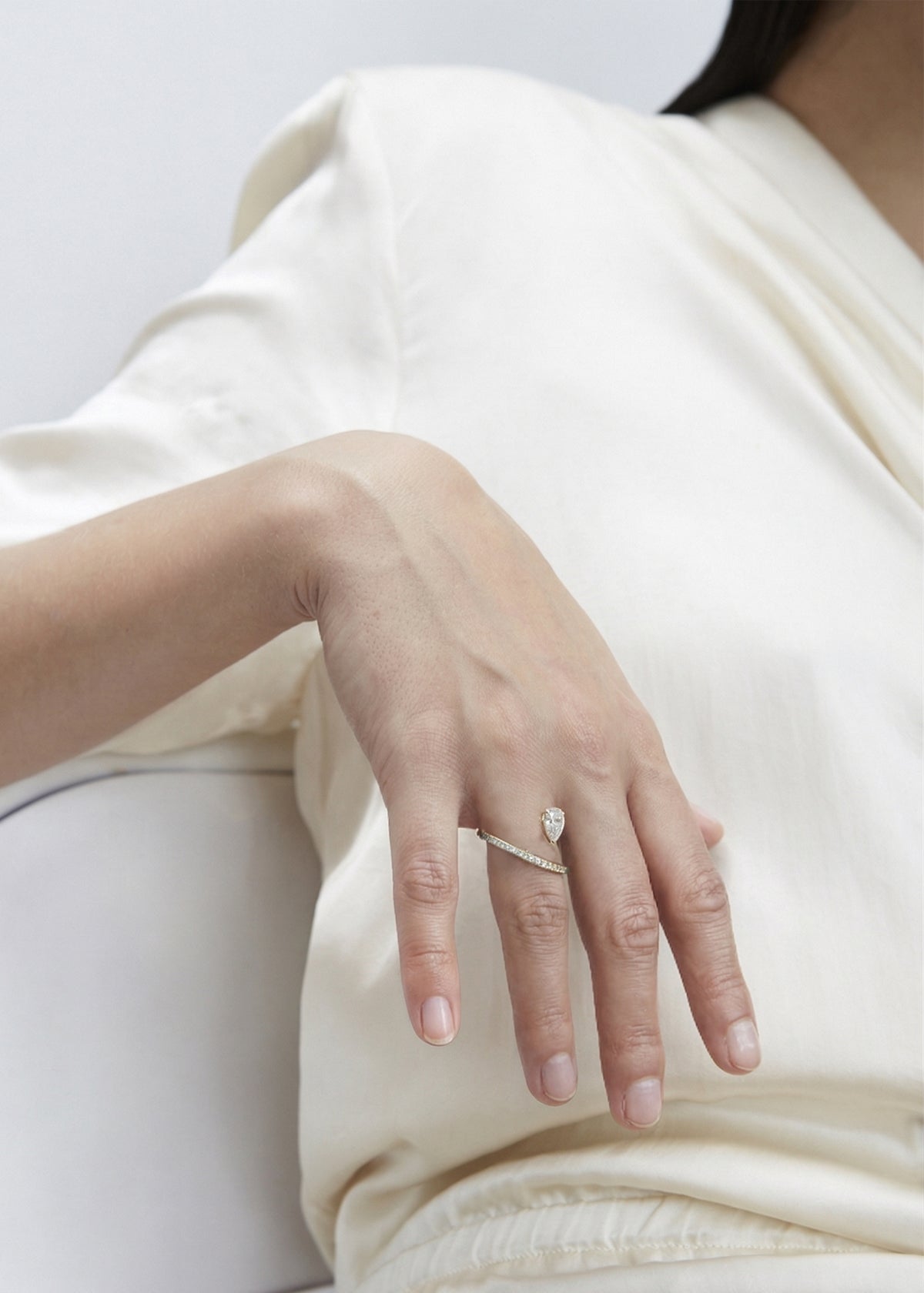close up of a hand wearing 18k yellow gold engagement ring featuring a floating pear cut diamond on an architectural tilted micropavé band.