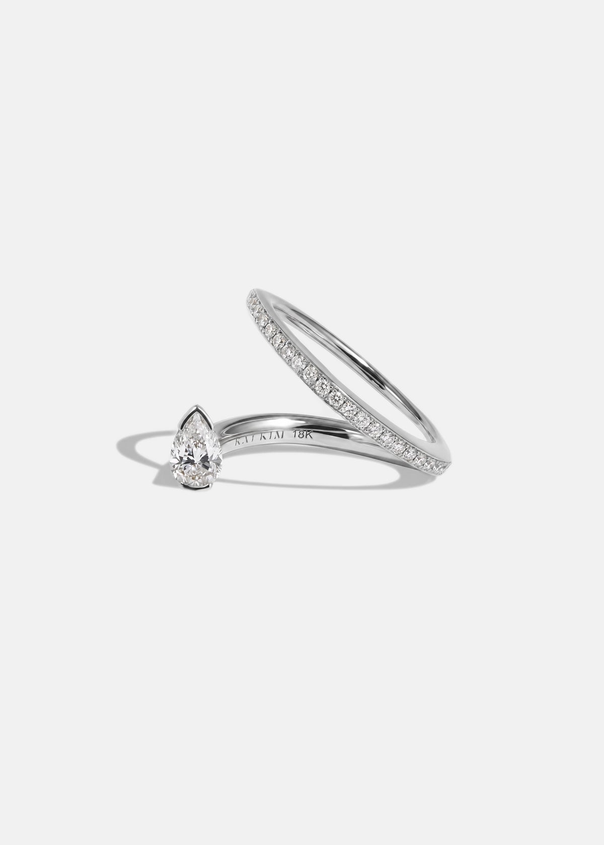 18k white gold engagement ring featuring a floating pear cut diamond on an architectural tilted micropavé band against a reflective surface.
