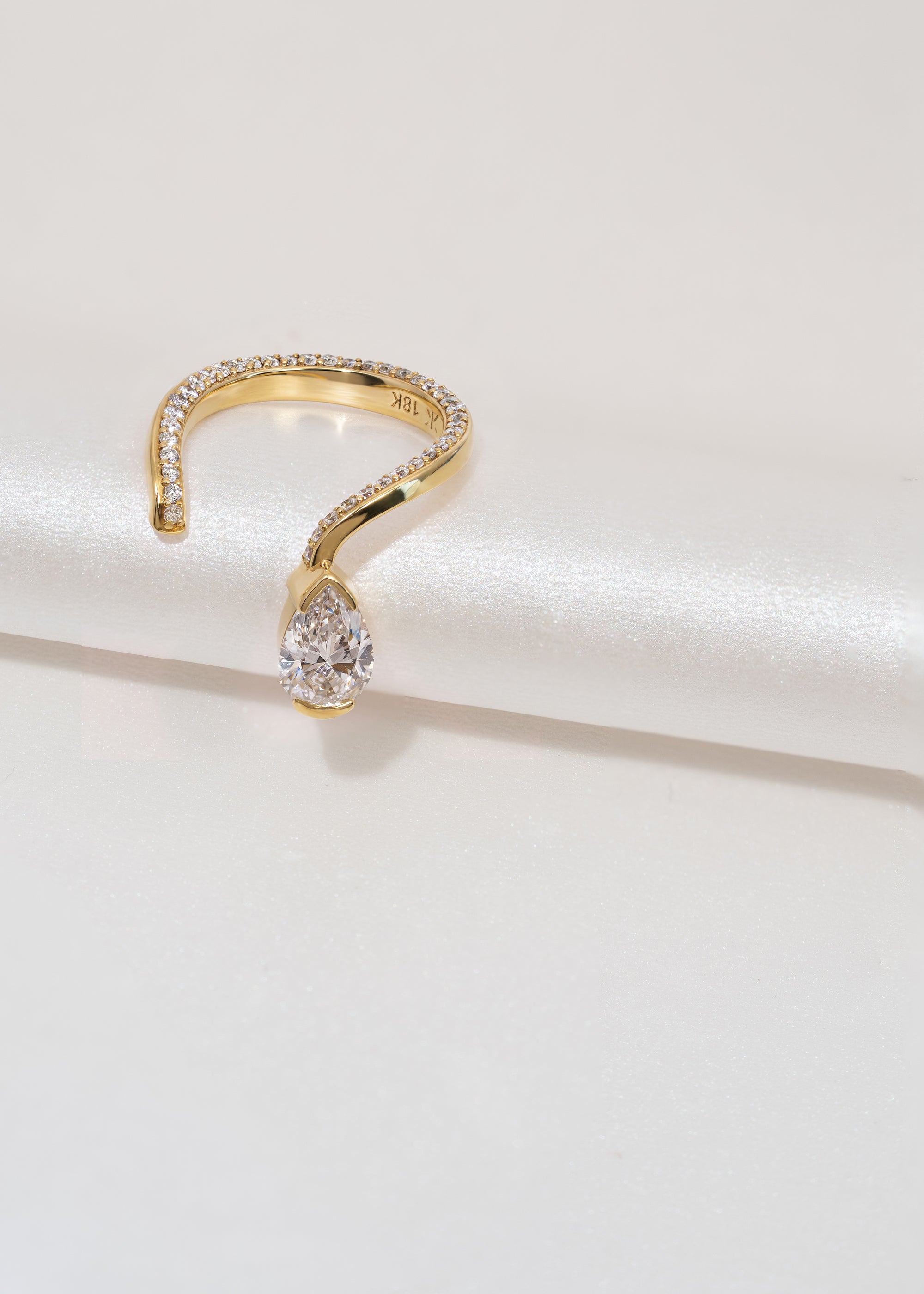 A 18k yellow gold open wrap ring featuring a pear-cut diamond and a pavé diamonds along the band.
