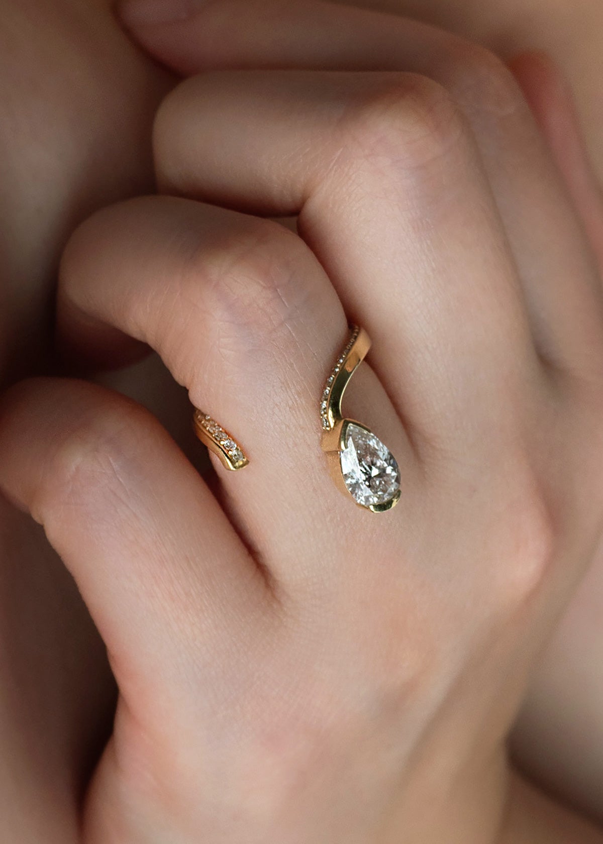 model wearing a 18k yellow gold open wrap ring featuring a pear-cut diamond and a pavé diamonds along the band.