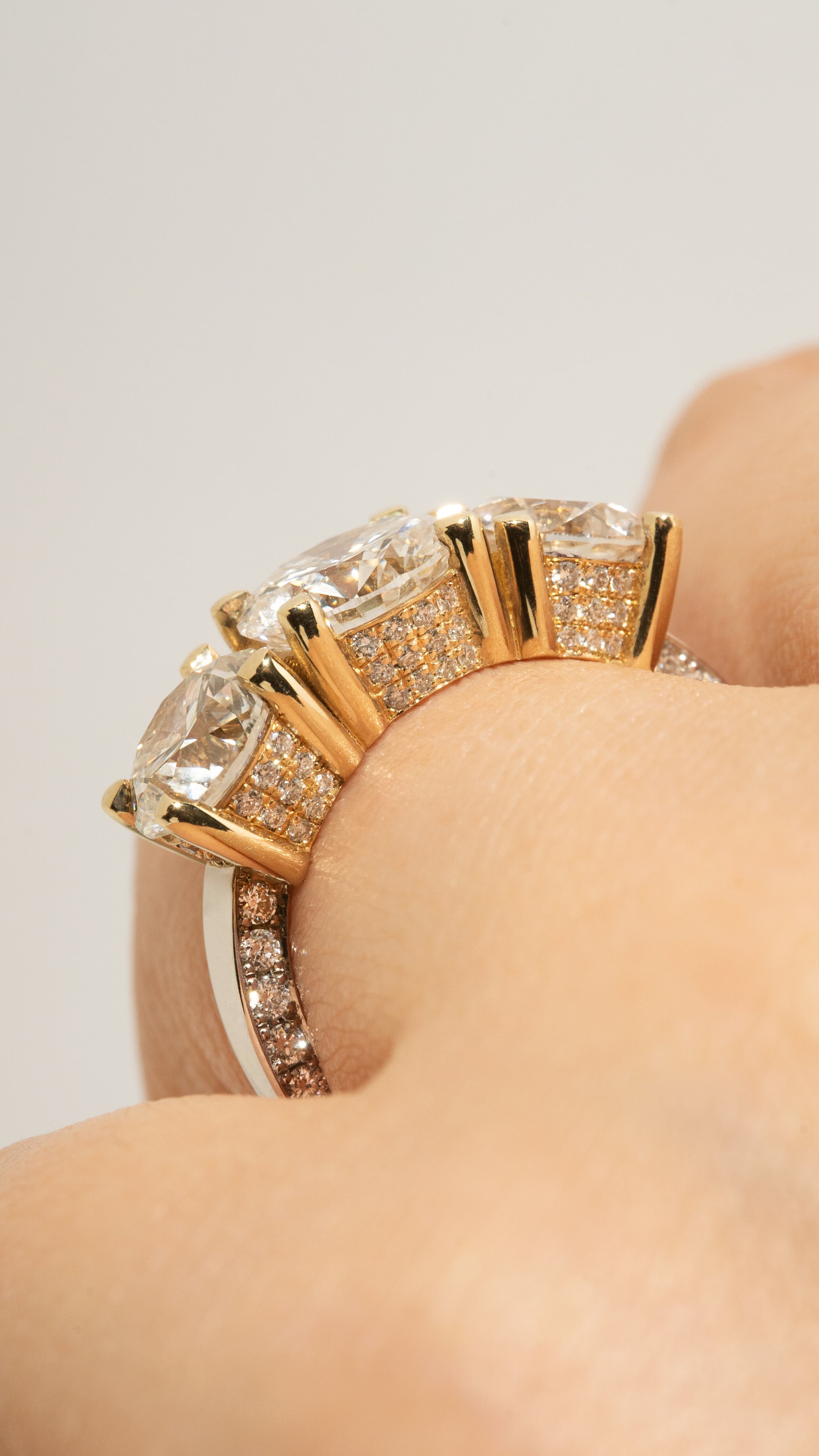 close-up of a hand wearing thin 18k white gold band with three round cut diamonds with halo pave diamonds.