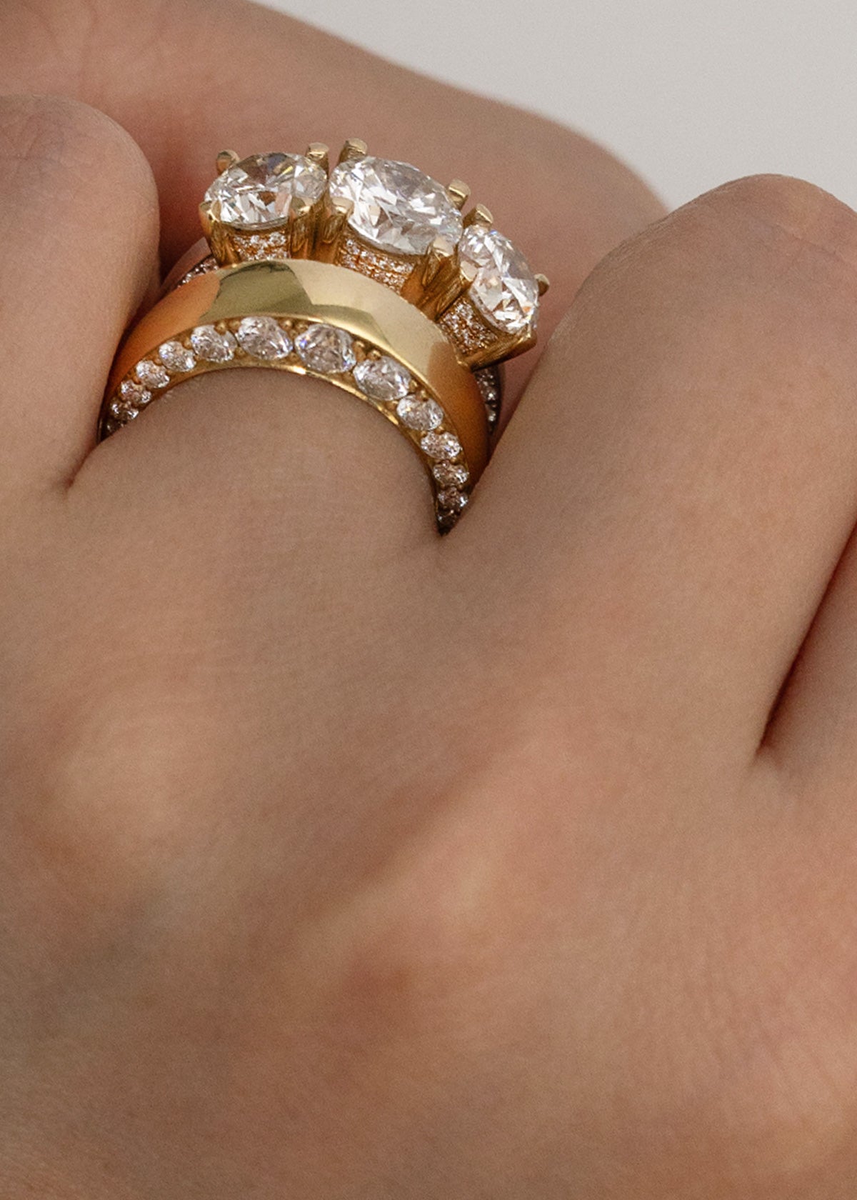 close-up of a hand wearing two rings, one is a thick gold band with tapering diamonds and another is thinner white gold band with three round cut diamonds.