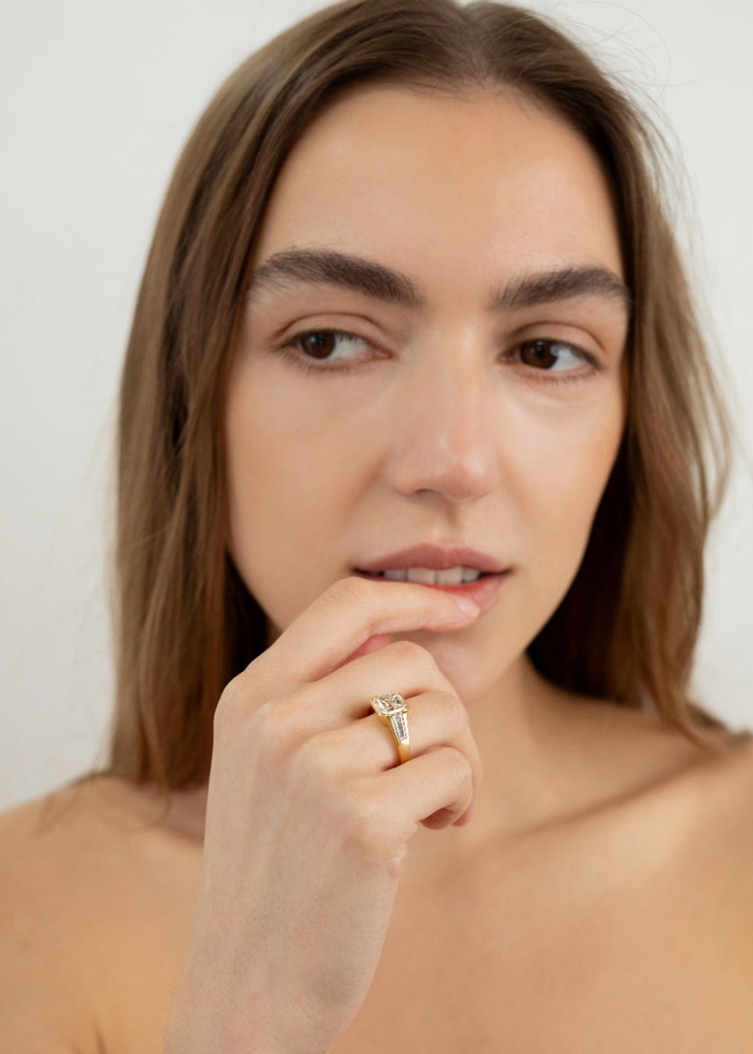 Model wearing the yellow gold ring featuring a central asscher-cut diamond flanked by two baguette-cut side stones 