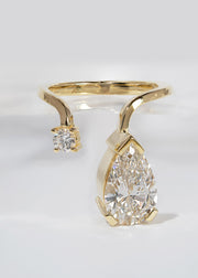A 18k yellow gold ring featuring a large pear-cut diamond drop and a smaller round diamond accent on a curved band.