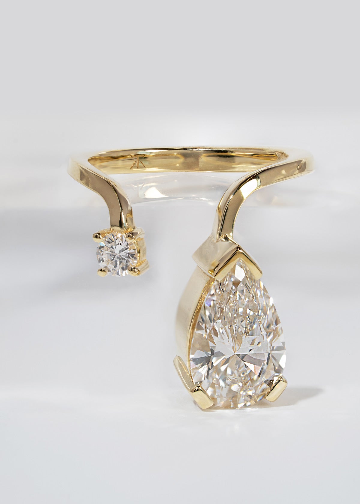 A 18k yellow gold ring featuring a large pear-cut diamond drop and a smaller round diamond accent on a curved band.