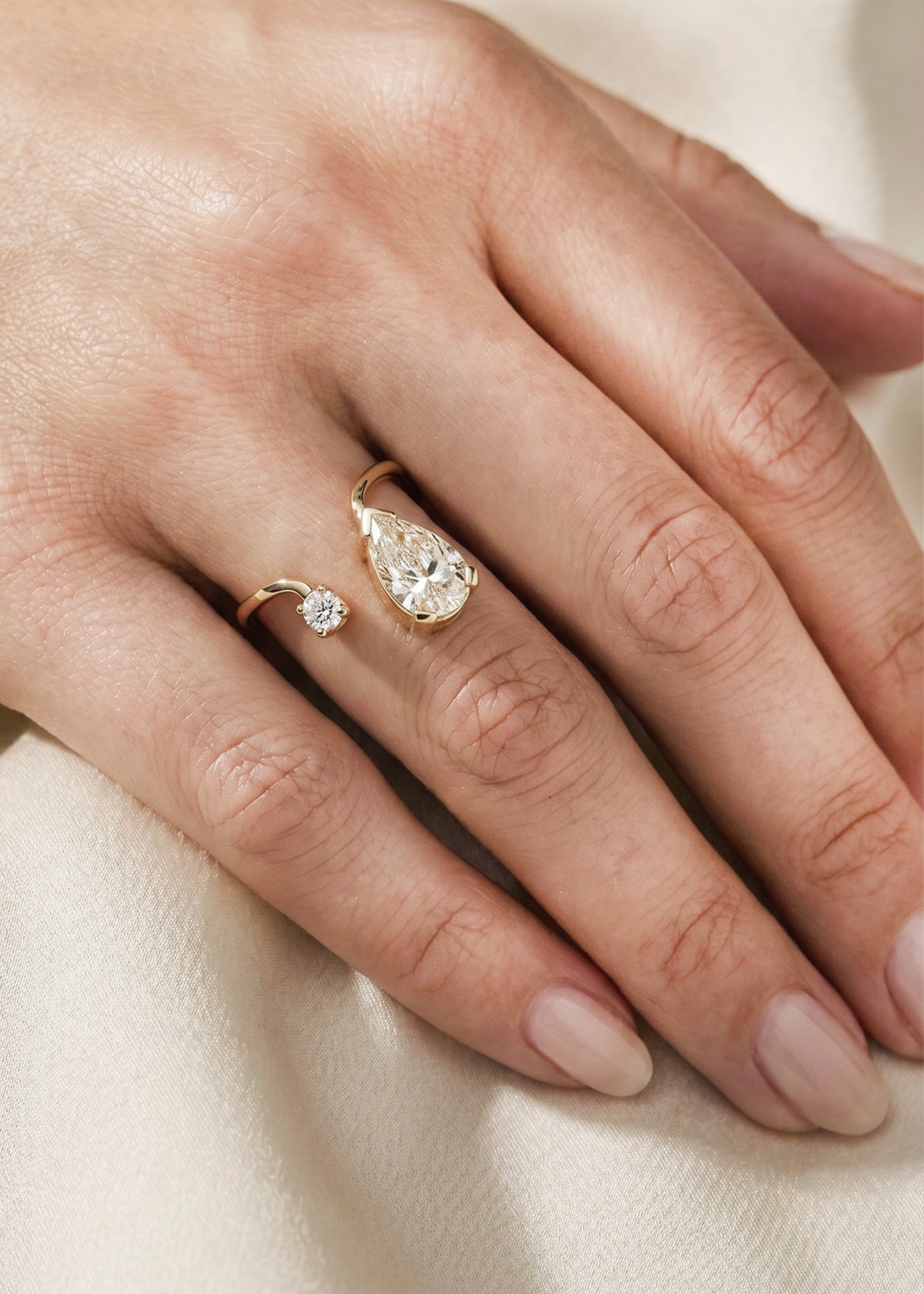 Hand wearing a 18k yellow gold ring with a pear-cut diamond and round cut diamond on curved band
