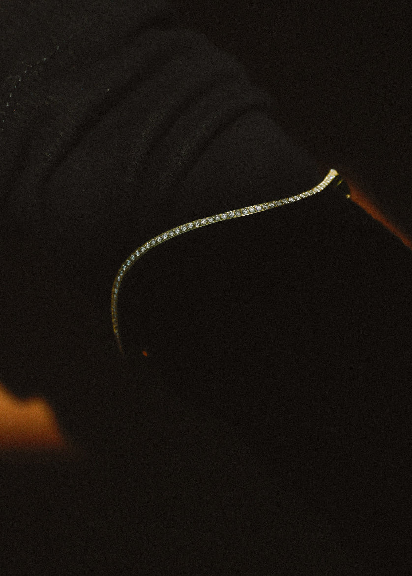 close up of a 18k yellow gold curved bracelet with pavé diamonds against a dark background