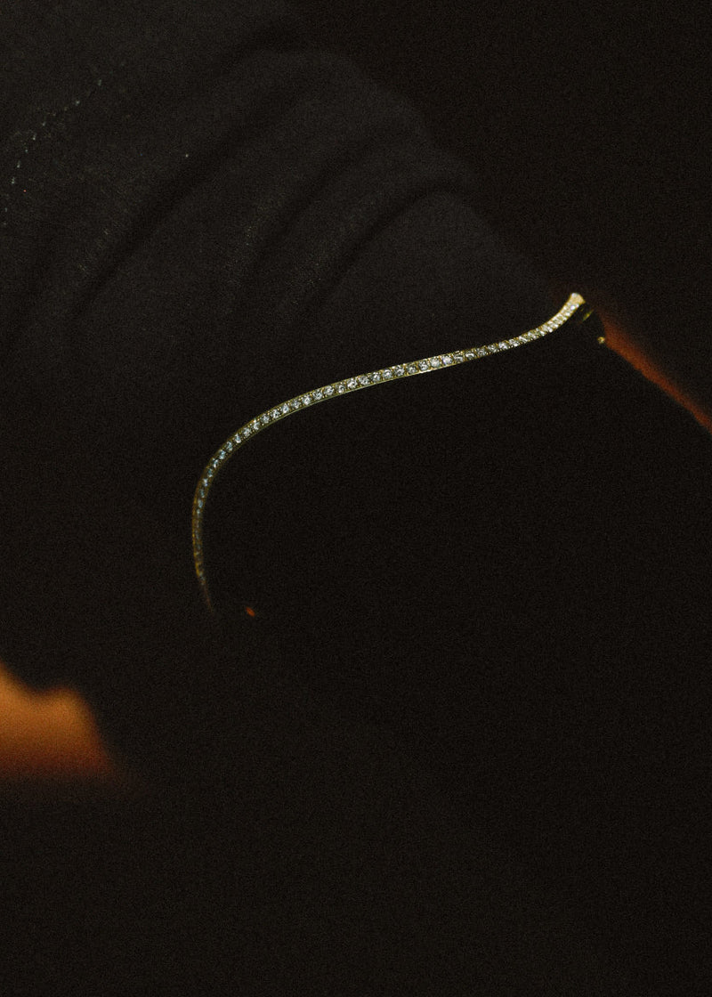 close up of a 18k yellow gold curved bracelet with pavé diamonds against a dark background