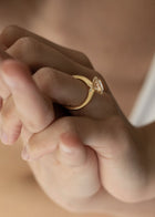 Close-up of a hand wearing a 18k yellow gold solitaire engagement ring featuring a oval cut diamond  accented by small pavé diamonds on the x-shaped shank.