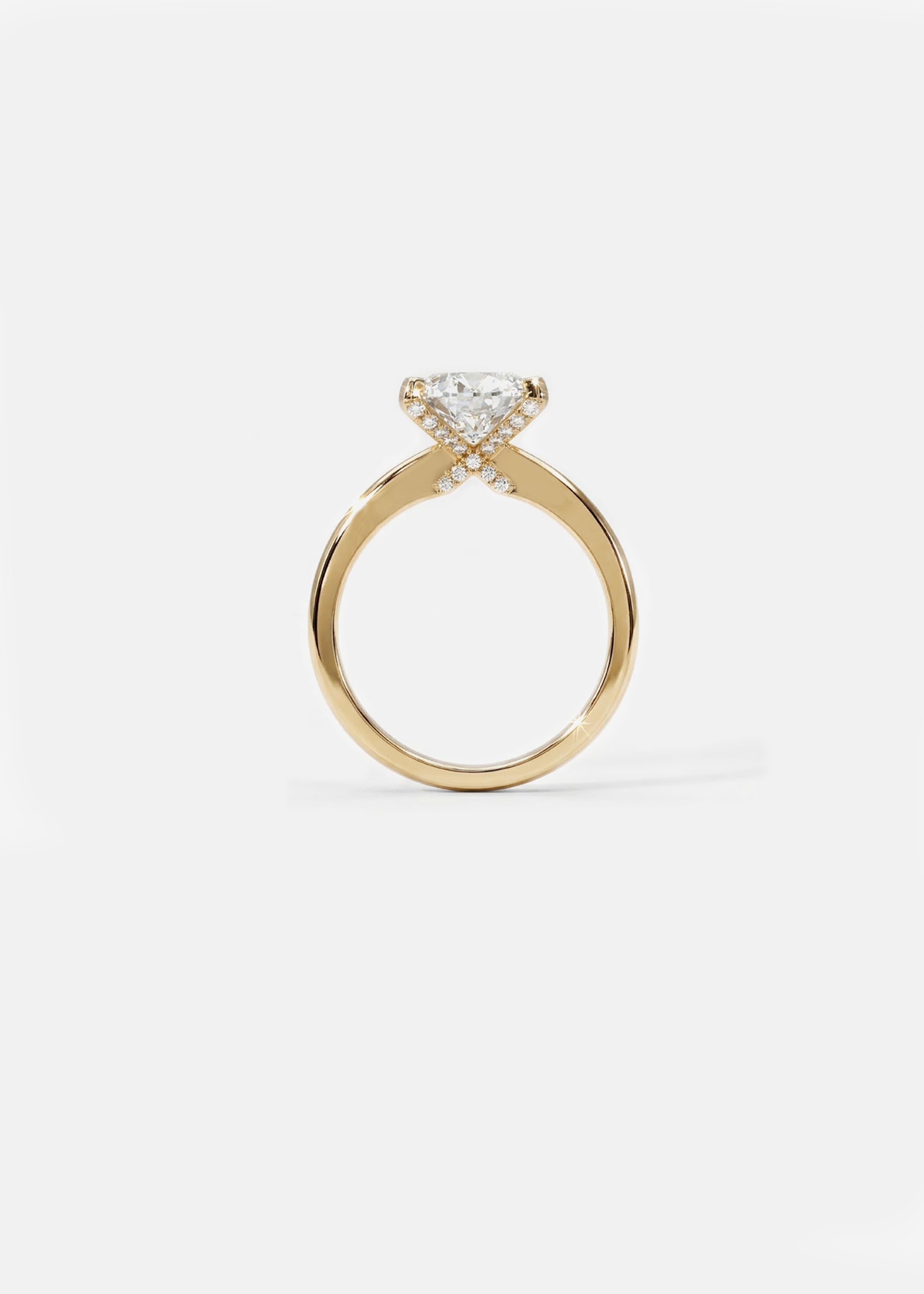A 18k yellow gold solitaire engagement ring featuring a oval cut diamond  accented by small pavé diamonds on the x-shaped shank.
