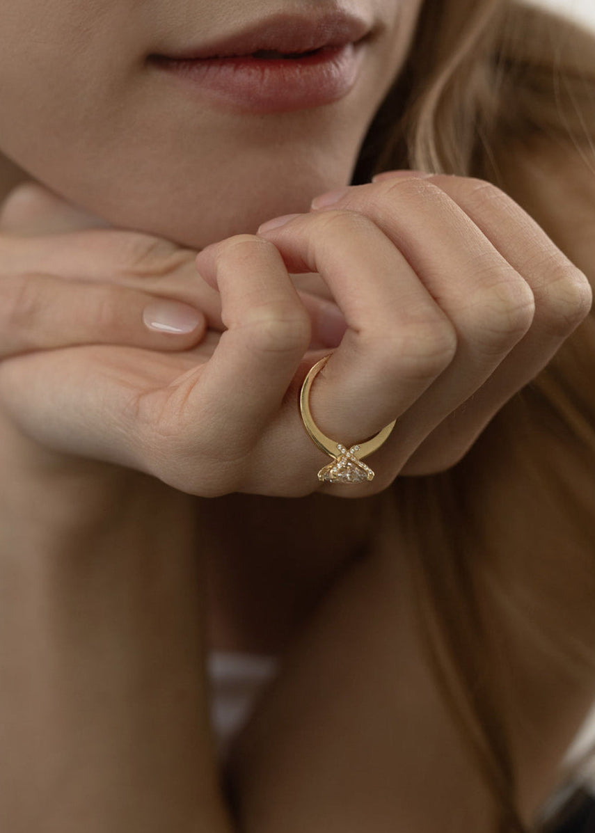 Close-up of a hand wearing a 18k yellow gold solitaire engagement ring featuring a oval cut diamond  accented by small pavé diamonds on the x-shaped shank.