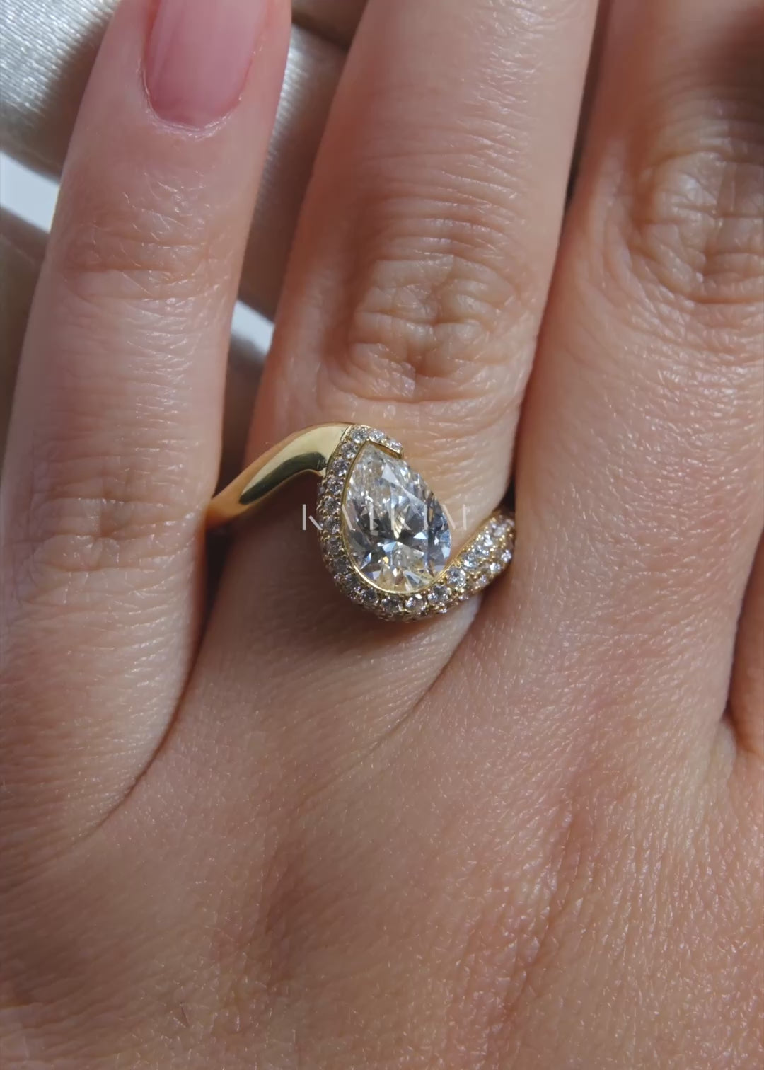 video of  18k yellow gold ring featuring a pear-cut diamond in a curved, wave-like setting with pavé diamonds around the center stone