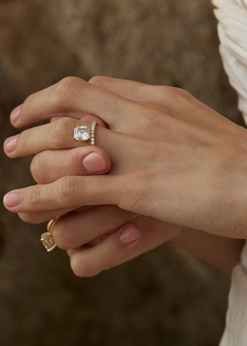 close-up of a hand wearing a 18k yellow gold engagement ring with a suspended floating asscher cut diamond and a pavé band