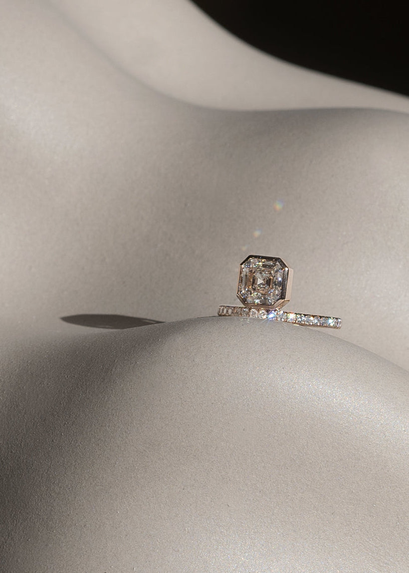 18k yellow gold engagement ring with a suspended floating asscher cut diamond and half pavé band along an asymmetrical white background