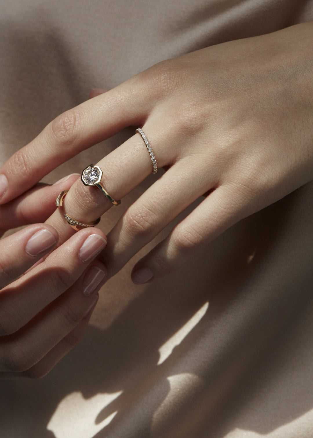 model wearing a deconstructed ring stack of 3 rings, center ring featuring 18k yellow gold architectural engagement ring with a round cut diamond in a thick, octagon bezel setting.