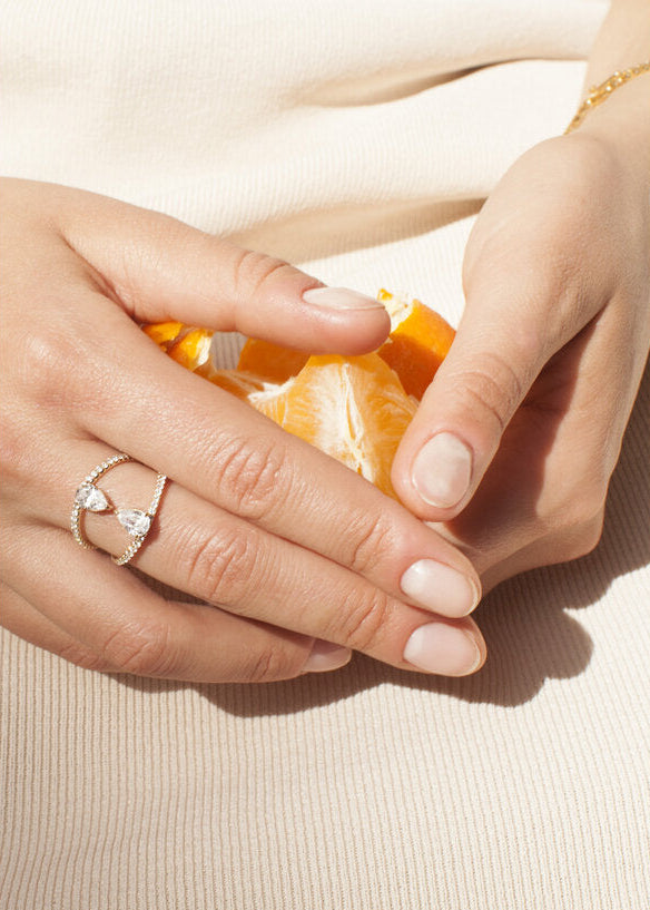 close up of a hand wearing 18k yellow gold dual engagement ring with two touching pear-cut diamonds facing opposite directions, with pavé diamonds along the band.