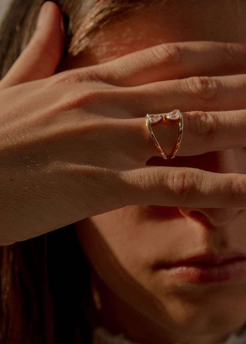 Close-up of a hand wearing a 18k yellow gold engagement ring with two touching pear-cut diamonds facing opposite directions..