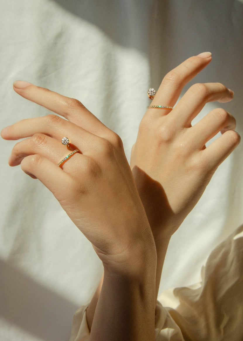 close-up of hands wearing male model wearing 18k yellow gold sculptural bypass ring featuring a floating round cut diamond accented by an unexpected tilted band silhouette with pavé diamonds on each hand.