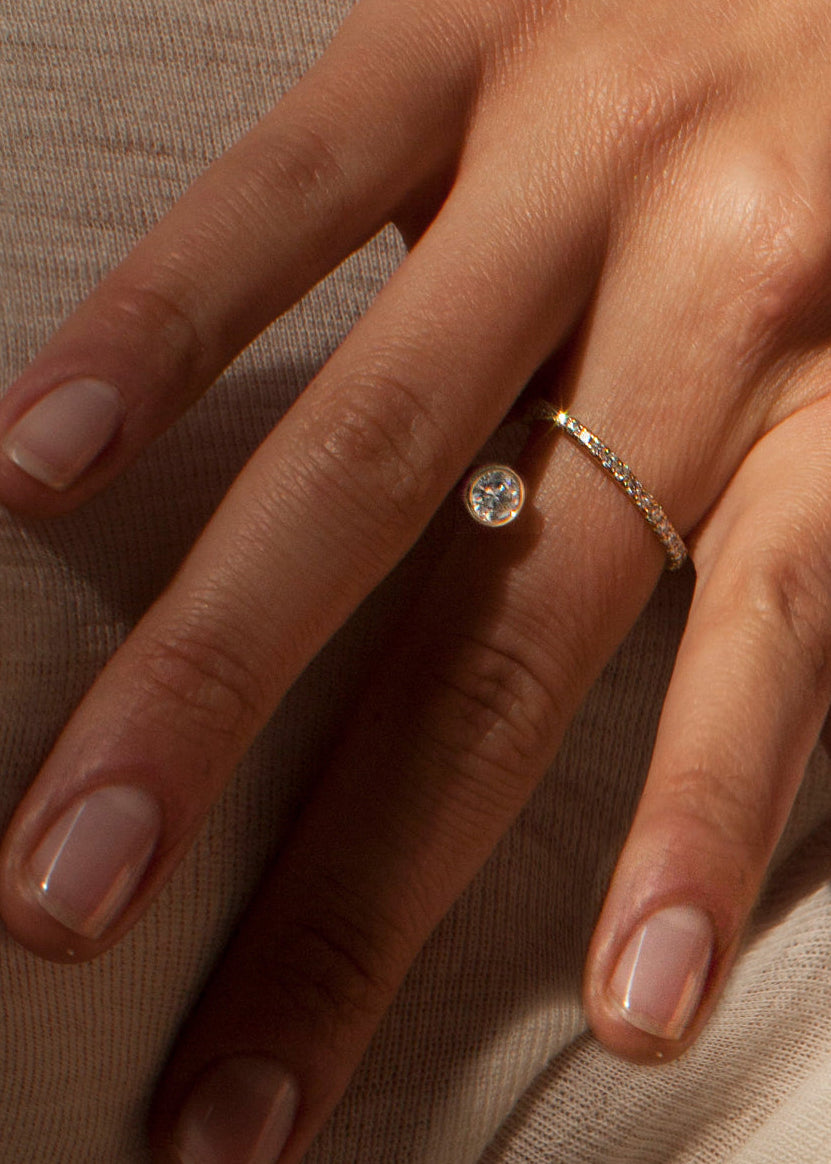 close up of a hand wearing 18k yellow gold sculptural bypass ring featuring a floating round cut diamond accented by an unexpected tilted band silhouette with pavé diamonds.