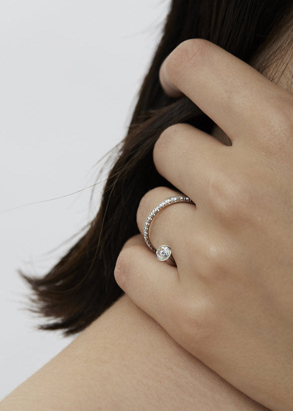 model wearing 18k white gold sculptural bypass ring featuring a floating round cut diamond accented by an unexpected tilted band silhouette with pavé diamonds.
